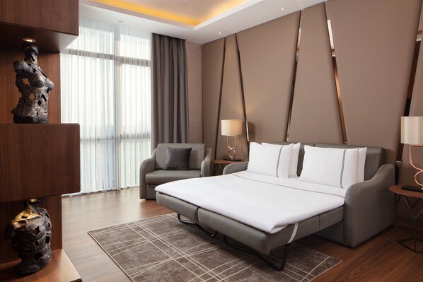 A modern hotel room with a large bed, two armchairs, a small table, and a decorative sculpture.