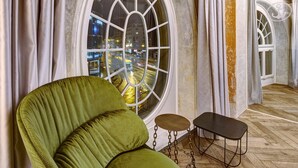 Una habitación con un amplio ventanal arqueado, un sillón tapizado en verde, una pequeña mesa redonda y suelo de madera.