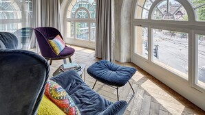 Una habitación moderna con amplios ventanales de arco, un sillón morado, un otoman azul y un sofá negro.