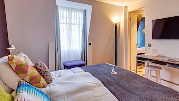 Habitación de hotel con cama, escritorio, televisión y ventana con cortinas.