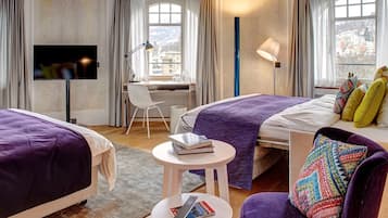 A hotel room with two beds, a desk, a chair, a small table, and a sofa.