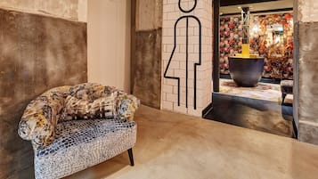 A modern interior with a patterned armchair, a minimalist wall art piece, and a decorative area with a large pot and floral wallpaper.