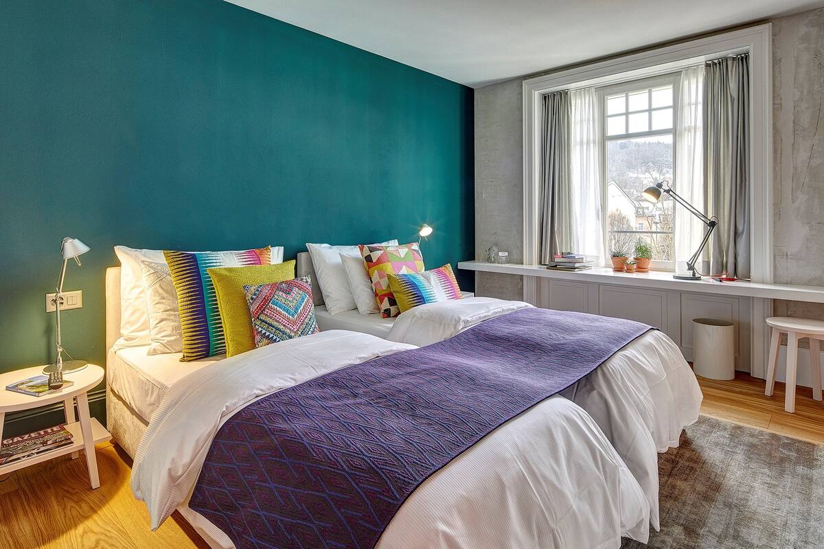 A bedroom with a bed, bedside table, lamp, and a window with curtains.