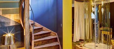 Una escalera de madera conduce a una habitación con una bañera y cabina de ducha con paredes de vidrio.
