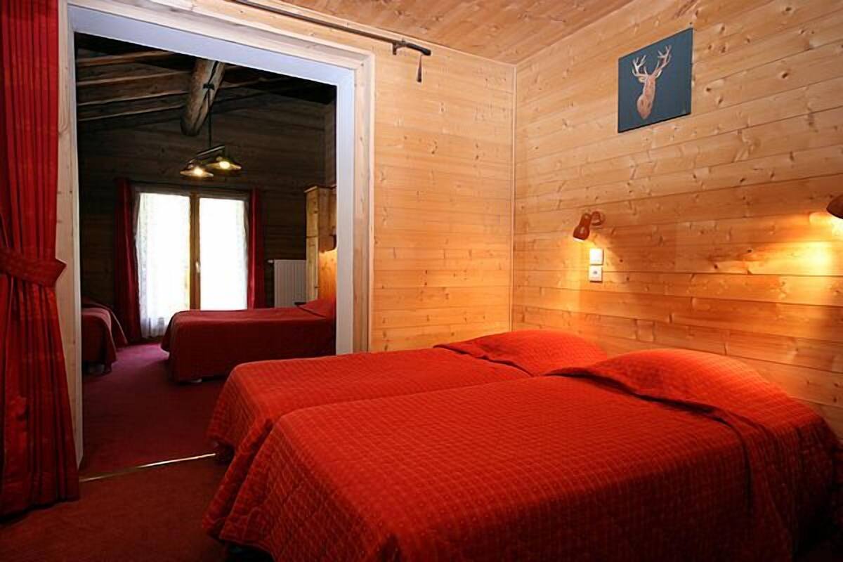 A room with two beds, wooden walls, a deer head picture, and a red curtain.