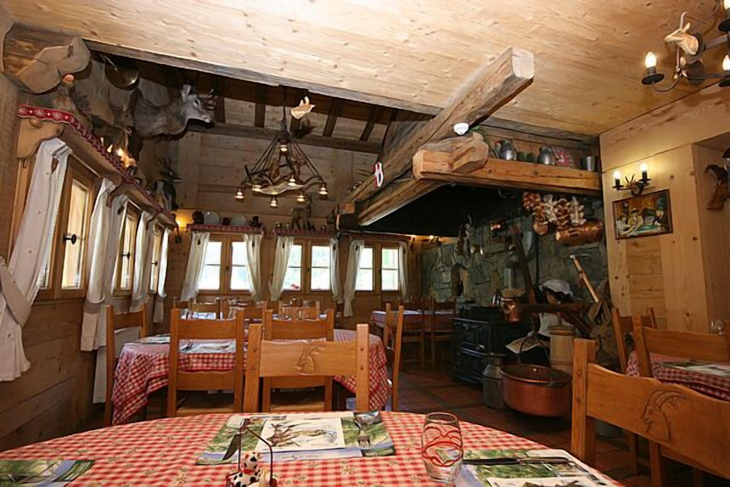 A rustic dining area with wooden tables and chairs, a chandelier, and a stone wall with various kitchen utensils.
