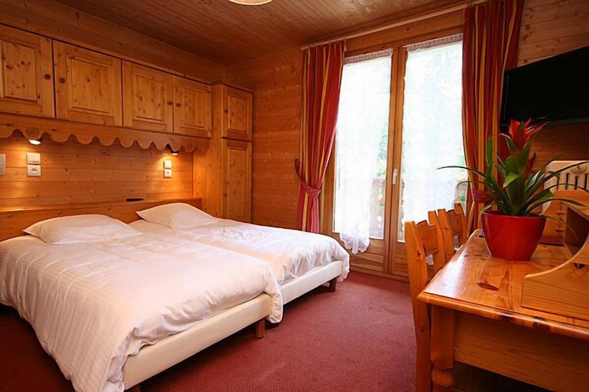 A wooden cabin room with two beds, a dining table, and a potted plant.