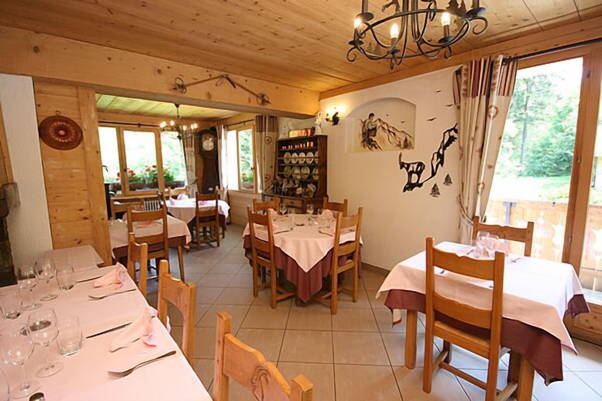 Ein Essbereich mit Holztischen und -stühlen, einer Deckenleuchte und einer Wand mit einer Dekorplatte sowie einem Regal mit Tellern.