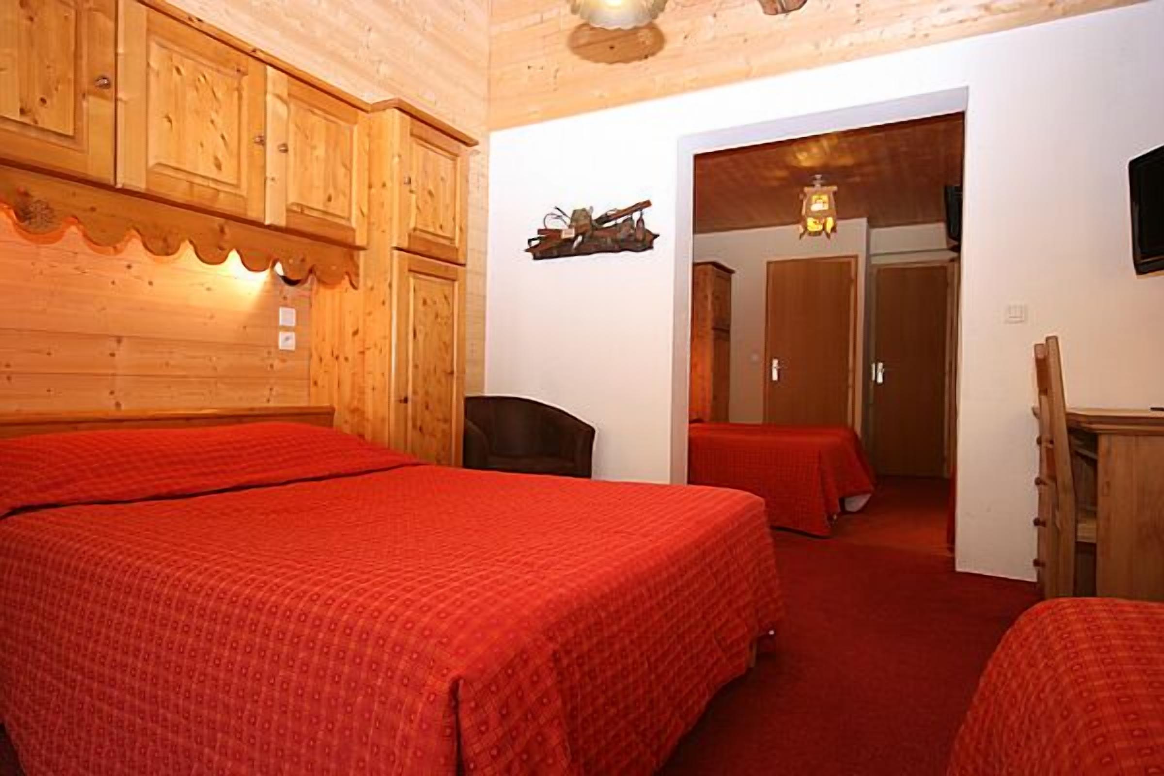 Une chambre avec deux lits, des murs en bois, un petit bureau et une porte donnant sur une autre pièce.