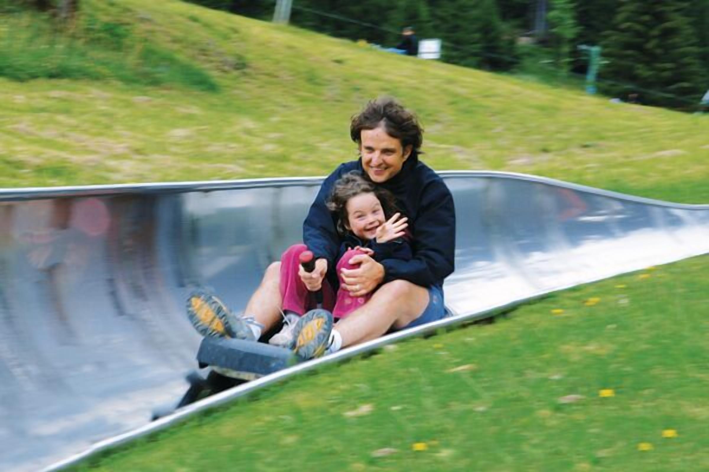 Une personne assise sur un toboggan métallique incurvé, dans un cadre extérieur.
