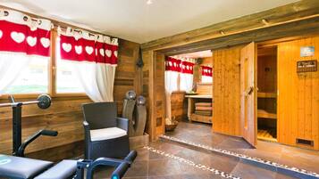 Une salle de sport équipée de matériel d’exercice, un fauteuil en osier et un espace sauna.