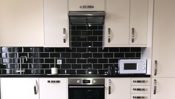 A modern kitchen with white cabinets, a black tiled backsplash, a microwave, and a stainless steel oven. - No 8 Apartments (Bristol)