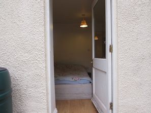 A narrow hallway leading to a bedroom with a bed, a window, and a hanging light fixture.