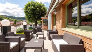 An outdoor seating area with wicker furniture, a large tree, and a view of the countryside. - Hôtel Burnichon (Vindry-sur-Turdine)
