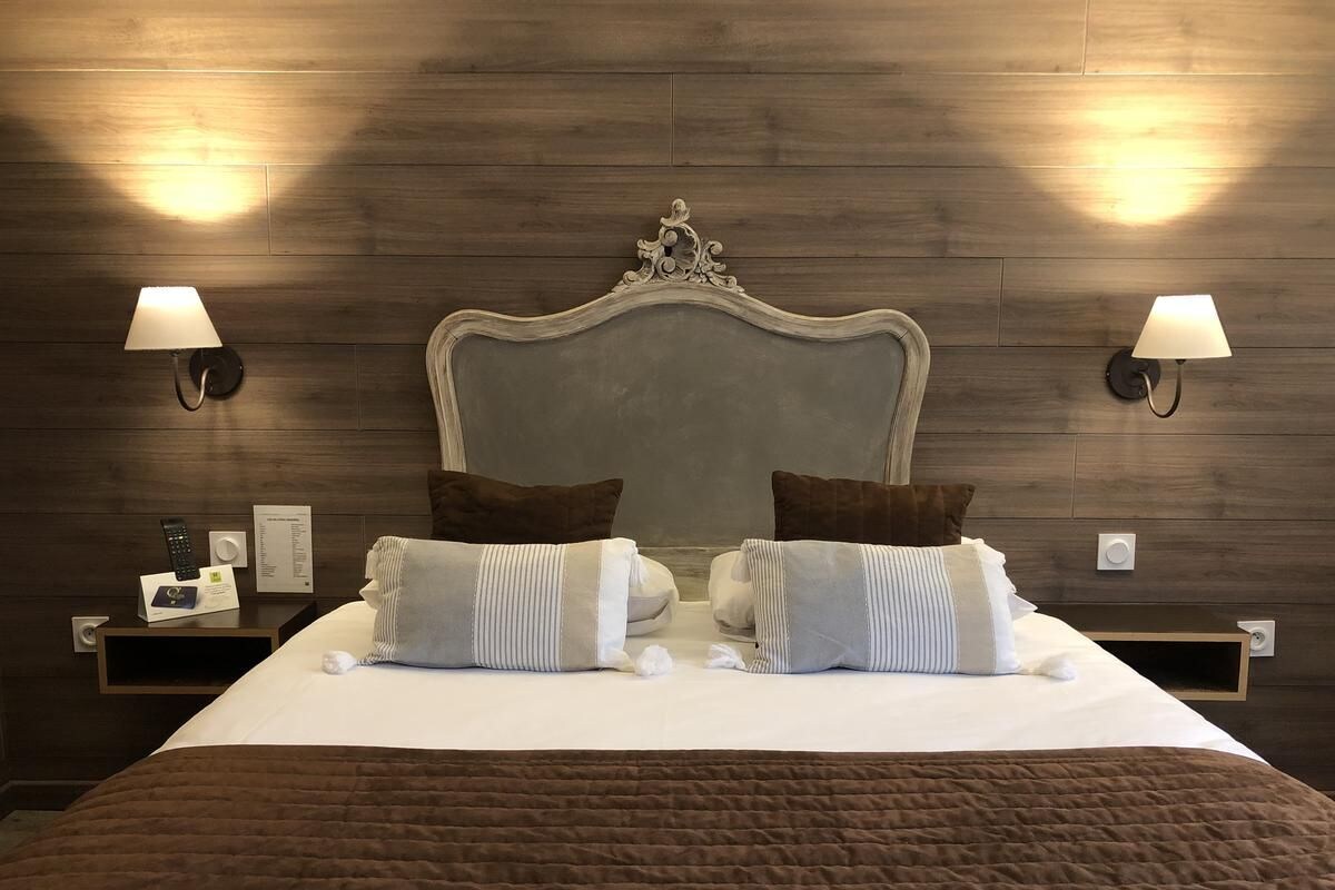 A hotel room with a large bed, two bedside tables, a headboard, and wall-mounted lamps.