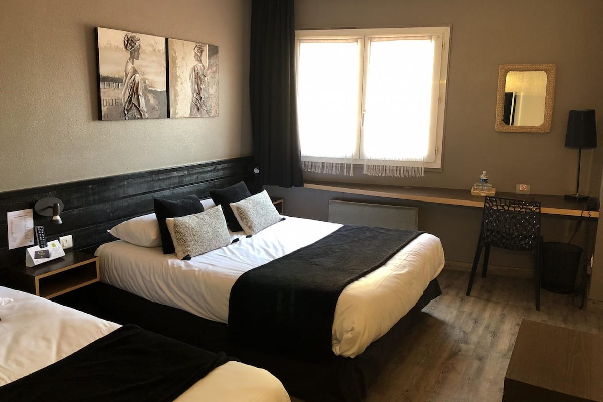 Habitación de hotel con dos camas, un escritorio, una silla, un ventanal grande y obras de arte en la pared.