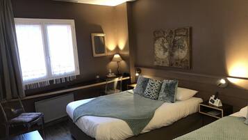 A hotel room with a large bed, a desk, a chair, a window with curtains, a map on the wall, and a lamp.