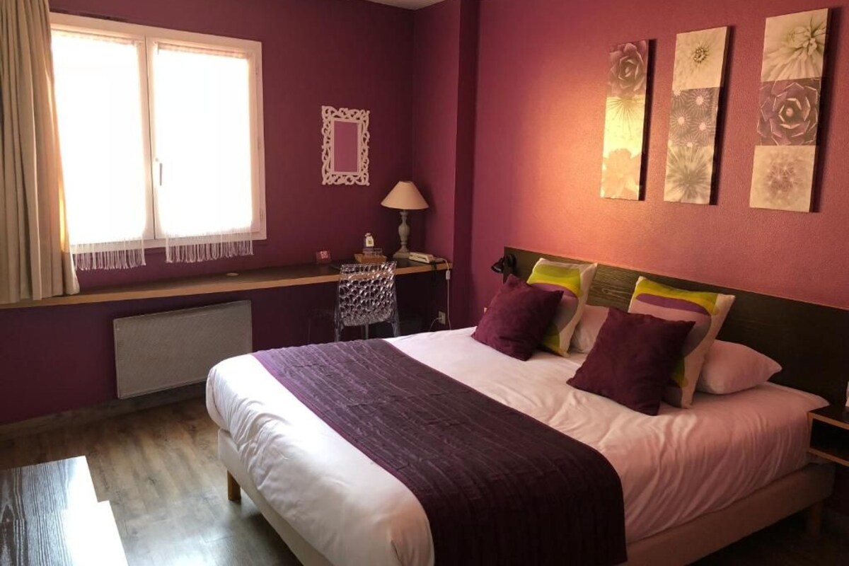 Un dormitorio con cama, mesita de noche, lámpara, ventana con cortinas y decoración en la pared.