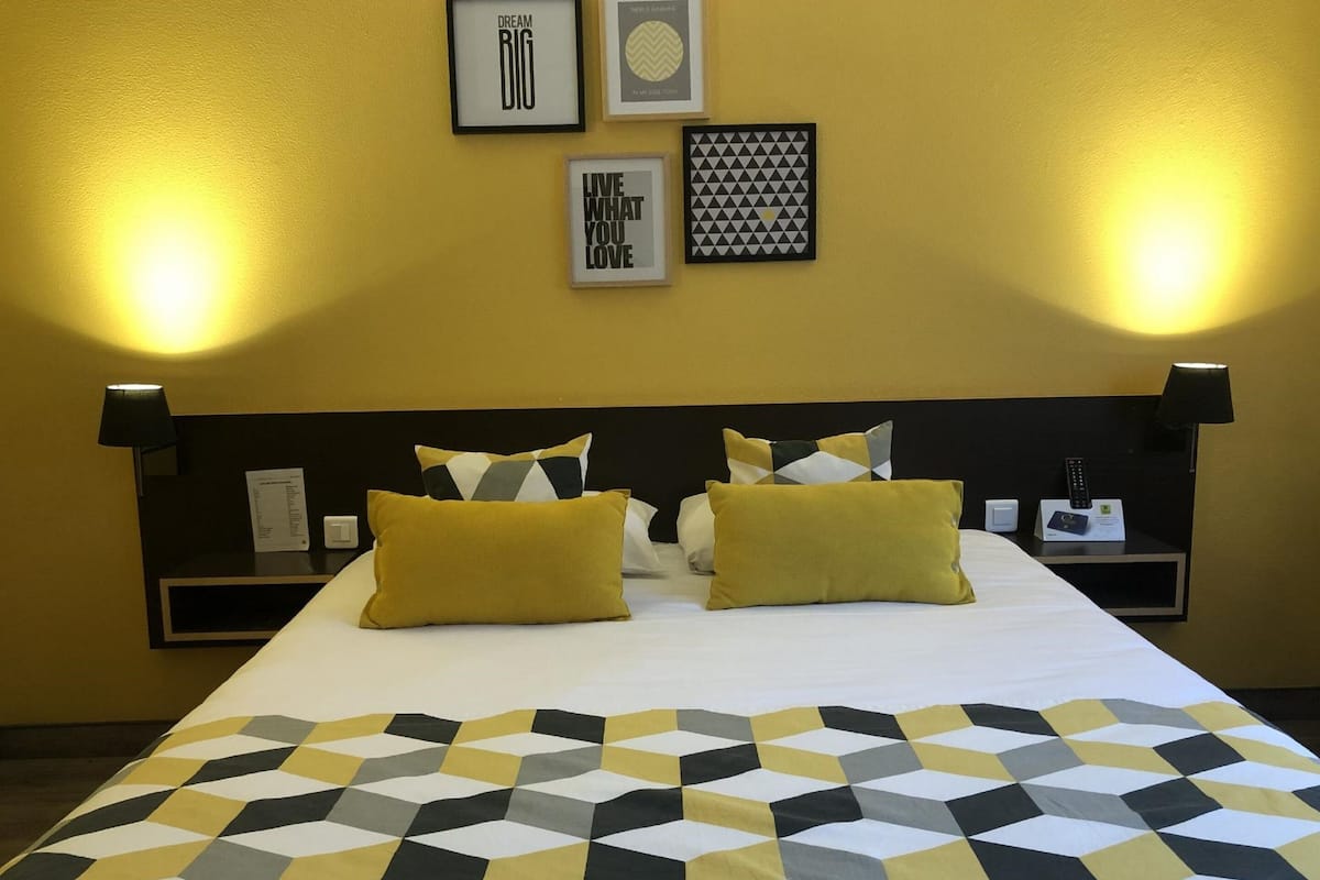 Habitación de hotel con una cama grande, dos mesitas de noche y tres carteles motivacionales enmarcados en la pared.