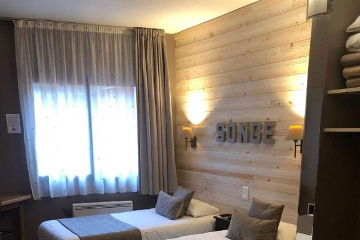 Habitación de hotel con dos camas, una pared de madera y una ventana con cortinas.