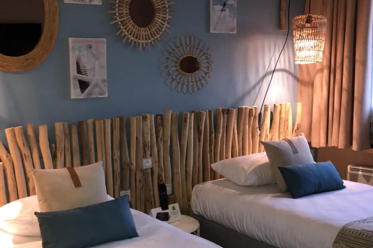 Una habitación con dos camas, cabecero de madera, decoración en la pared y una lámpara colgante.