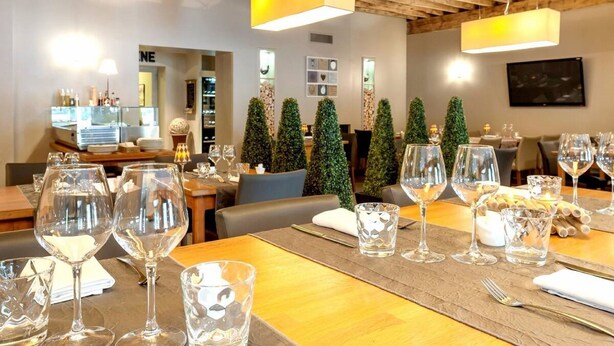 A restaurant interior with wooden beams, tables set with wine glasses, and decorative greenery. - Hôtel Burnichon (Vindry-sur-Turdine)