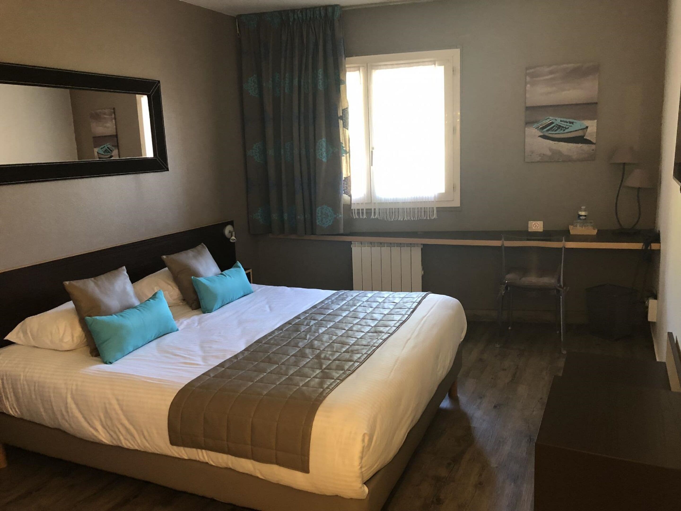 A hotel room with a large bed, a desk, and a window with curtains.