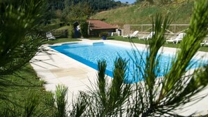 A swimming pool with lounge chairs, surrounded by greenery and a small building. - Hôtel Burnichon (Vindry-sur-Turdine)