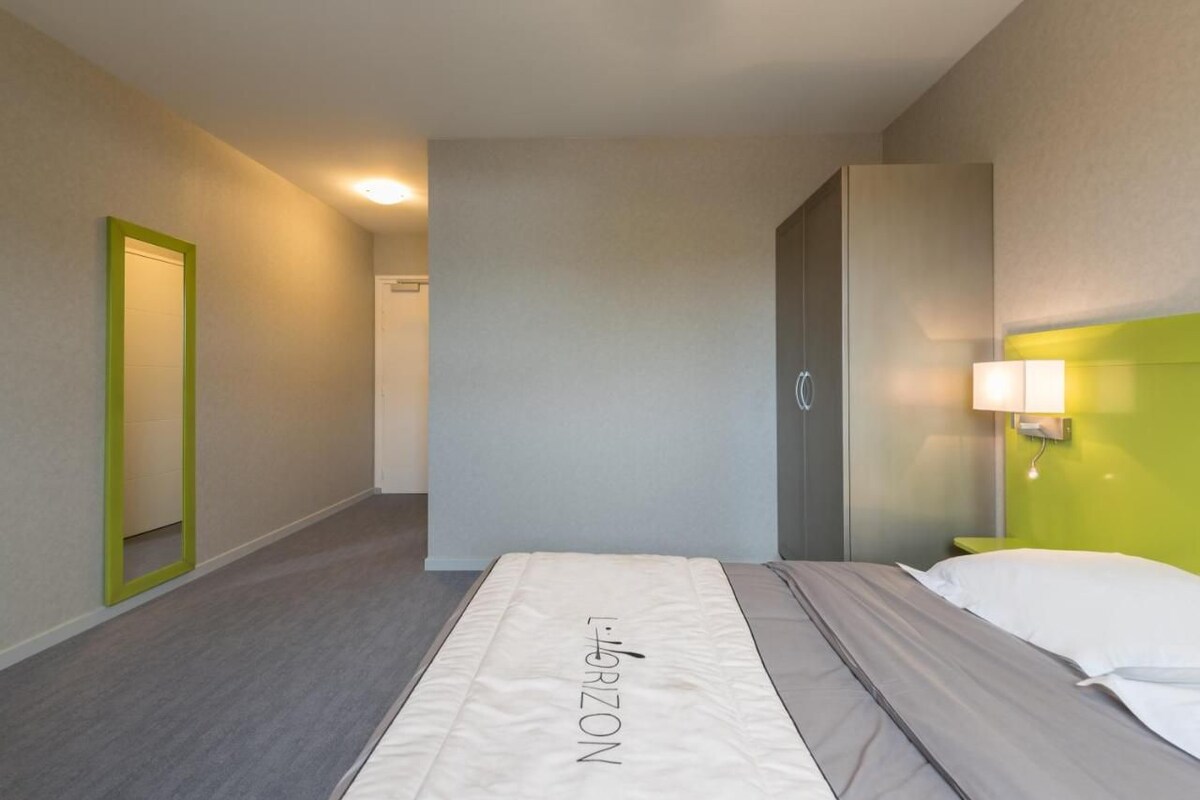 Ein Hotelzimmer mit Bett, Spiegel, Tür und Nachttisch mit Lampe.