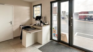 A reception area with a desk, a computer, and a window with a view of the street. - Hôtel l'Horizon (Saint-Symphorien-sur-Coise)