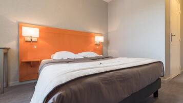 A hotel room with a bed, a nightstand, and a wall-mounted lamp.