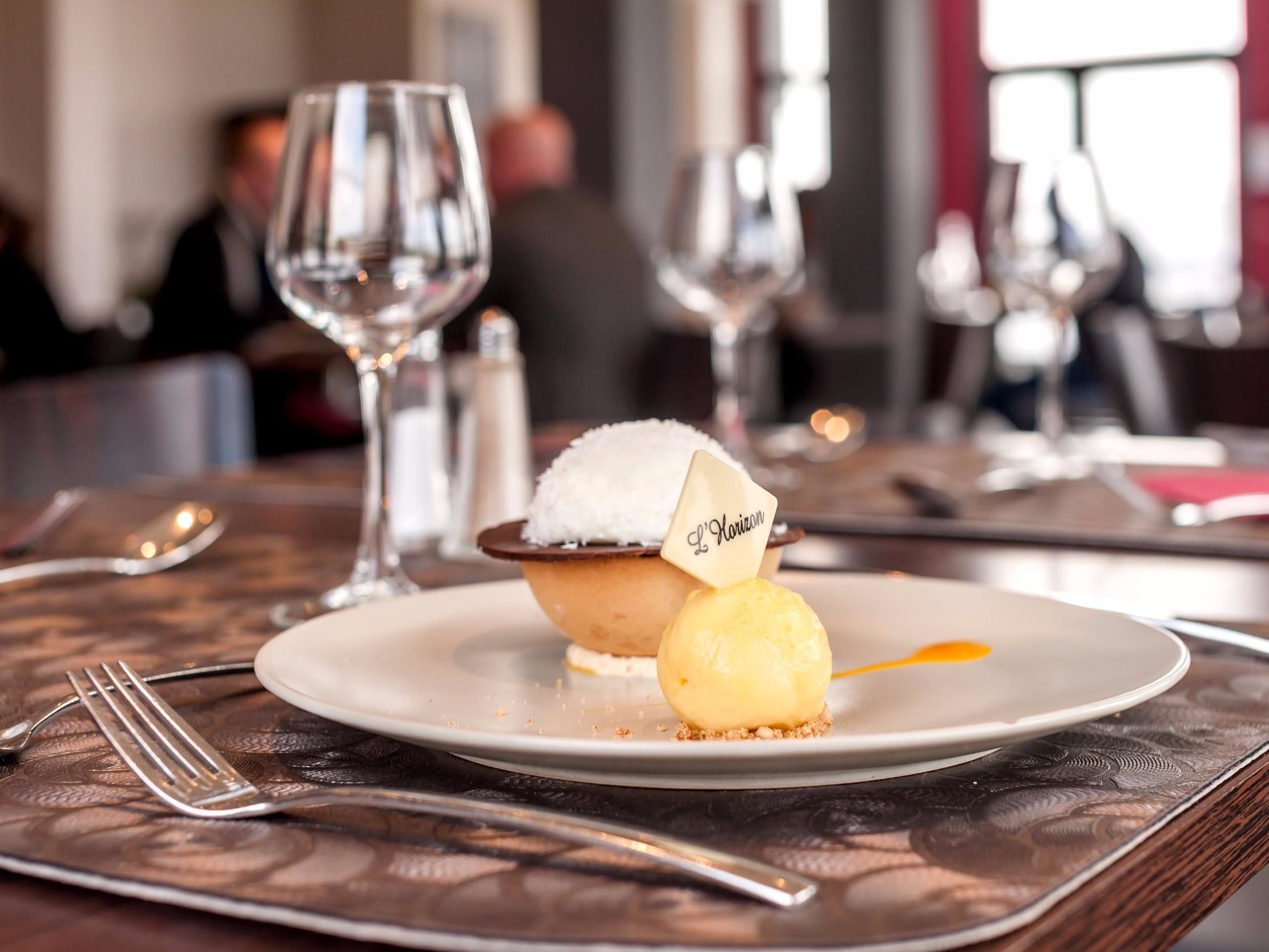 A dessert on a plate with a label, a fork, and a glass of water on a table.