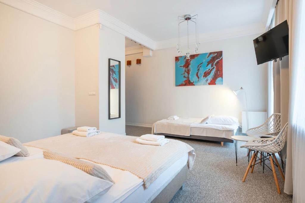 A hotel room with two beds, a flat-screen TV, a painting, and a chair.