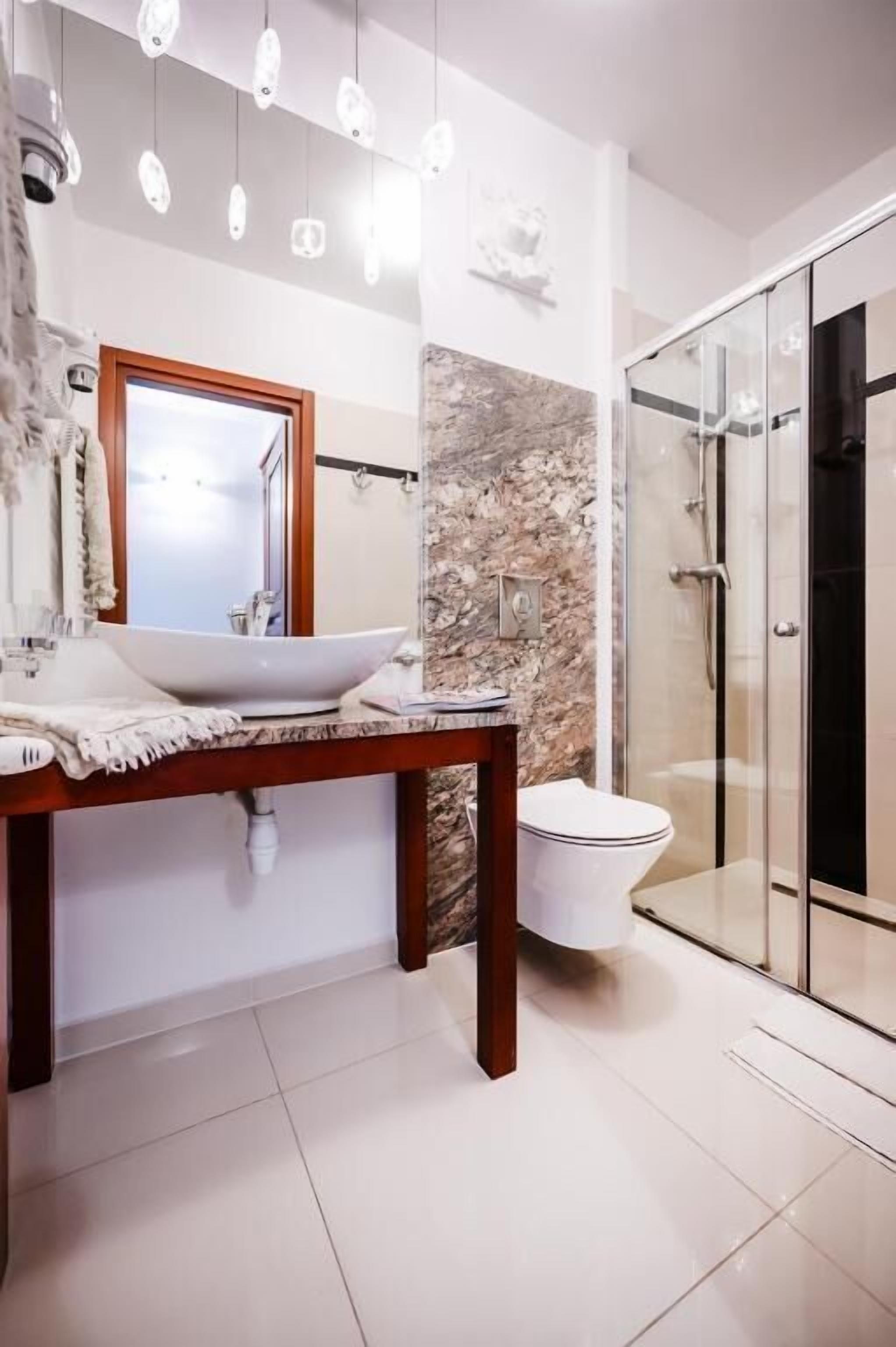 Une salle de bain moderne avec un mur en marbre, un lavabo blanc et une cabine de douche en verre.