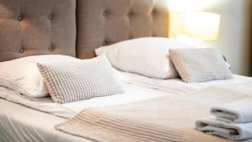 A neatly made bed with a tufted headboard, white linens, and a folded towel on the side.