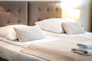 A neatly made bed with a tufted headboard, white linens, and a folded towel on the side.