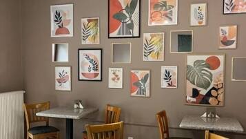 A dining area with wooden chairs and tables, a chandelier, and various framed artworks on the walls.