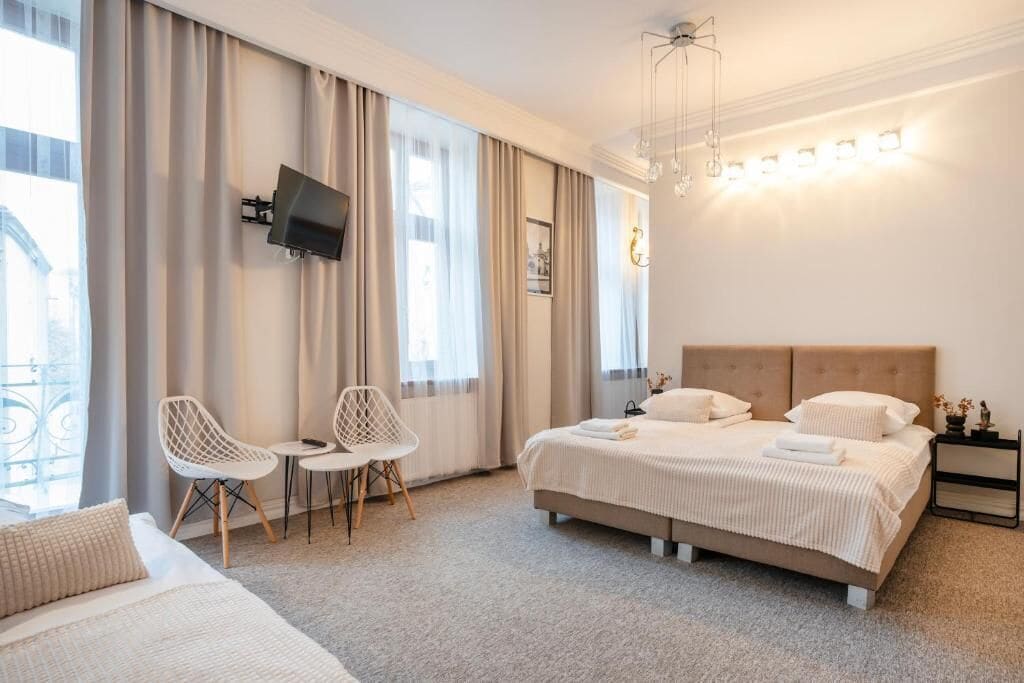 Una habitación de hotel con una cama, dos sillas, un televisor y una mesita de noche.