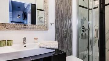 Un baño moderno con un espejo grande, lavamanos blanco, encimera negra y una cabina de ducha de vidrio.