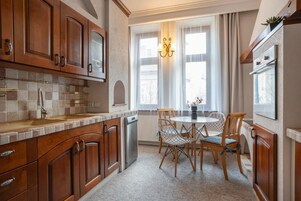 A kitchen with wooden cabinets, a tiled backsplash, a dishwasher, a dining table with chairs, and a window with curtains.