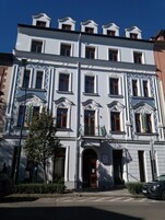 A multi-story building with a classic architectural style, featuring a central entrance with a decorative archway and multiple windows with wooden frames.