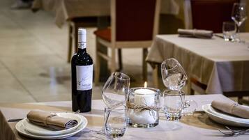 A dining table set with plates, cutlery, a wine bottle, and candle-lit glasses.