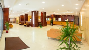 A modern hotel lobby with a reception desk, seating area, and a large potted plant. - BV President Hotel (Rende)