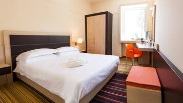 Een hotelkamer met een bed, een bureau, een stoel, een kledingkast en een raam.