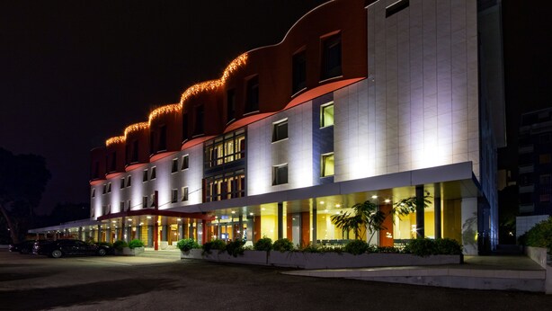 A multi-story hotel with a modern design, featuring a prominent entrance with a covered walkway and outdoor seating area. - BV President Hotel (Rende)