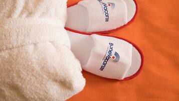 A pair of white slippers with red trim and the logo 'BunyanVacances' on a textured orange fabric.