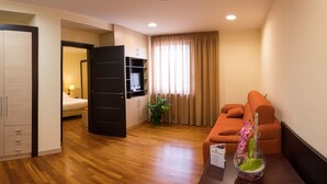 A hotel room with a wooden floor, a bed, a TV on a shelf, a sofa, and a sign with room amenities. - BV President Hotel (Rende)