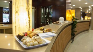 A reception area with a marble column, a counter displaying pastries, and a reception desk with a plant. - BV President Hotel (Rende)