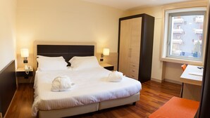 A hotel room with a large bed, bedside lamps, a wardrobe, a desk, and a window with a view of buildings. - BV President Hotel (Rende)
