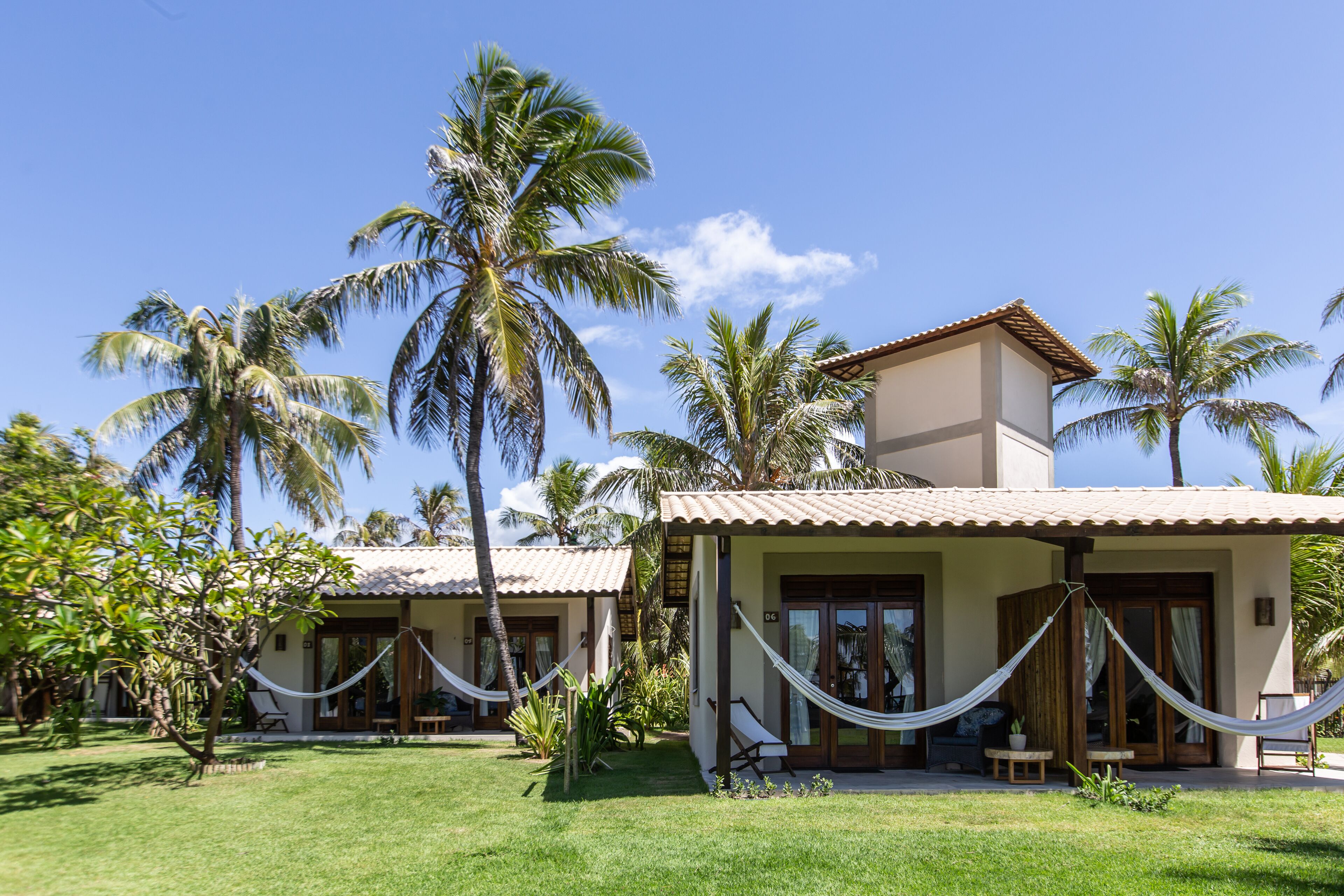 A resort with two villas, each featuring a covered patio with a hammock, surrounded by lush greenery and palm trees.